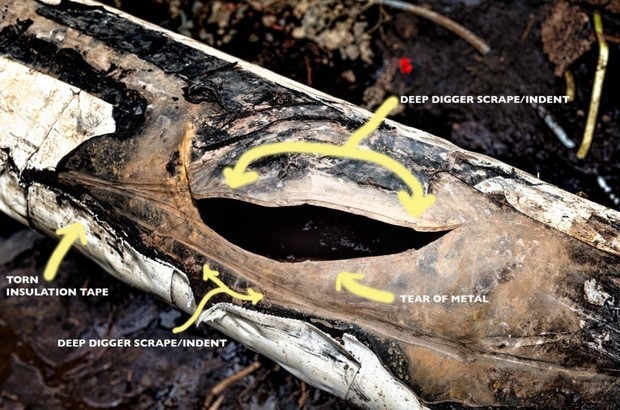 A photograph showing the damaged section of the pipeline in situ following excavation. This damage mainly consists of a large crescent shaped tear in the metal pipe. Also highlighted on the picture are 2 deep digger scrapes/indents and some torn insulation tape. A photograph showing the damaged section of the pipeline in situ following excavation. This damage mainly consists of a large crescent shaped tear in the metal pipe. Also highlighted on the picture are 2 deep digger scrapes/indents and some torn insulation tape.
